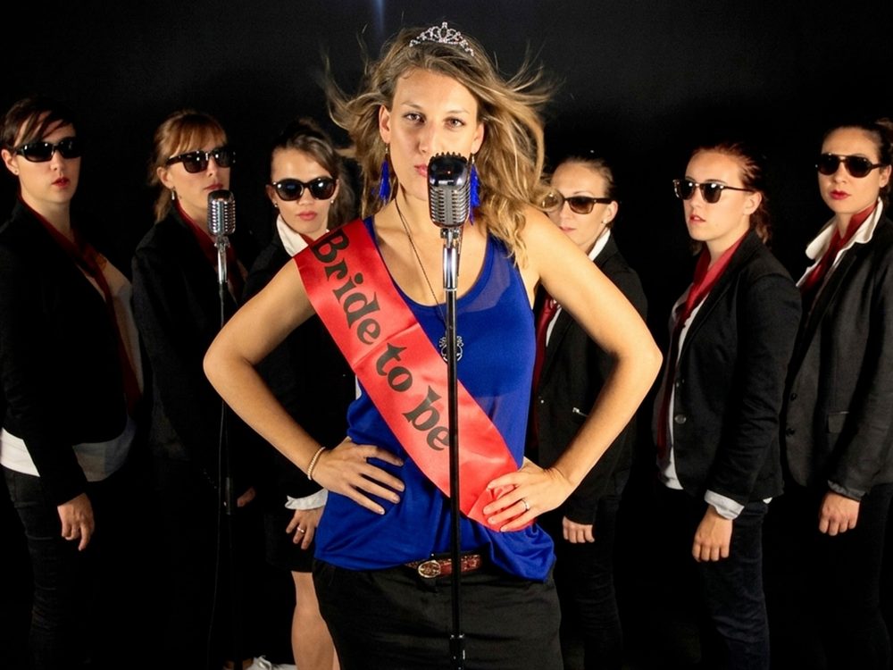 Tournage sur fond noir : une chanteuse au micro vintage, le groupe aligné derrière elle